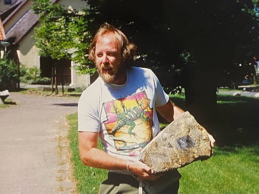 A man holds up a slab of rock.