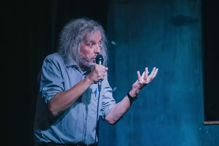 man with long grey hair talks into microphone