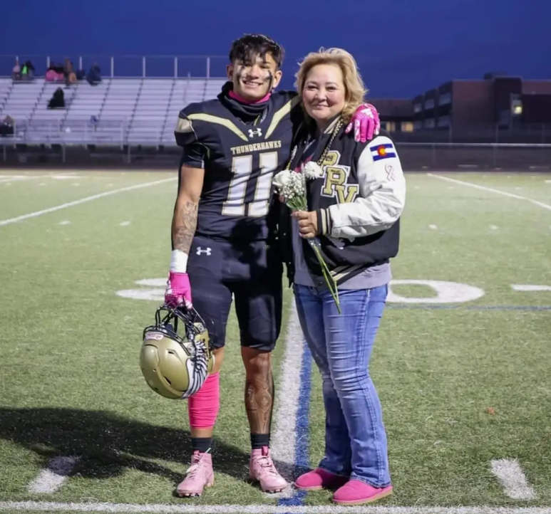 a boy on football gear posing with a woman