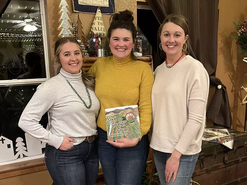 three women posting with a book
