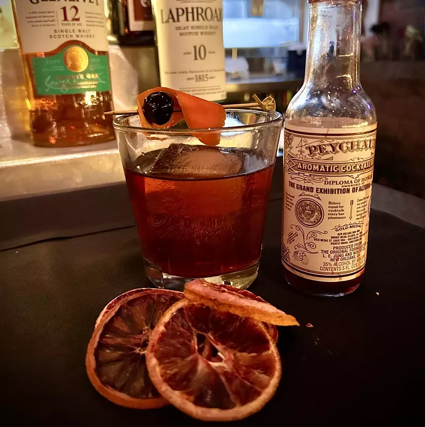 a cocktail in a glass garnished with orange and cherry