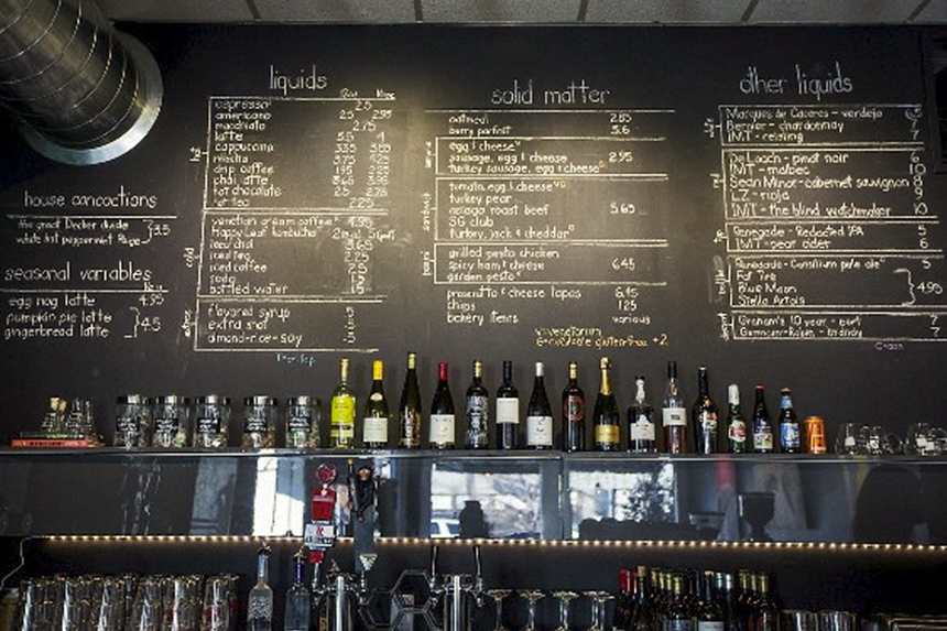 a menu handwritten on a chalkboard above wine bottles