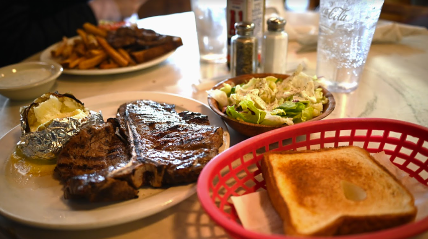 bread in a red basket, a steak on a plate and a salad in a bowl