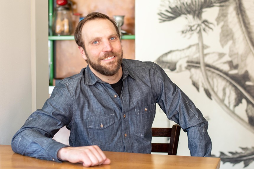 a man in a blue buttons down short posing at a table