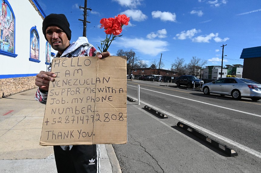 A Venezuelan migrant stands with a sign and roses.
