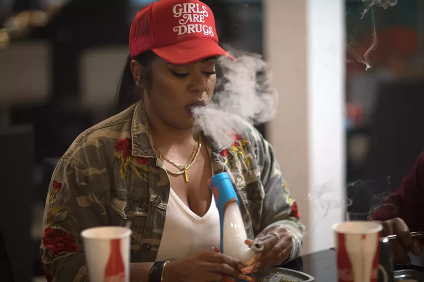 A woman blows out a hit of marijuana smoke from a bong