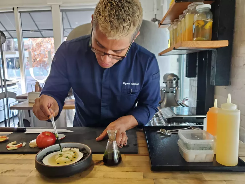 a man in a blue chef's coat plating a dish