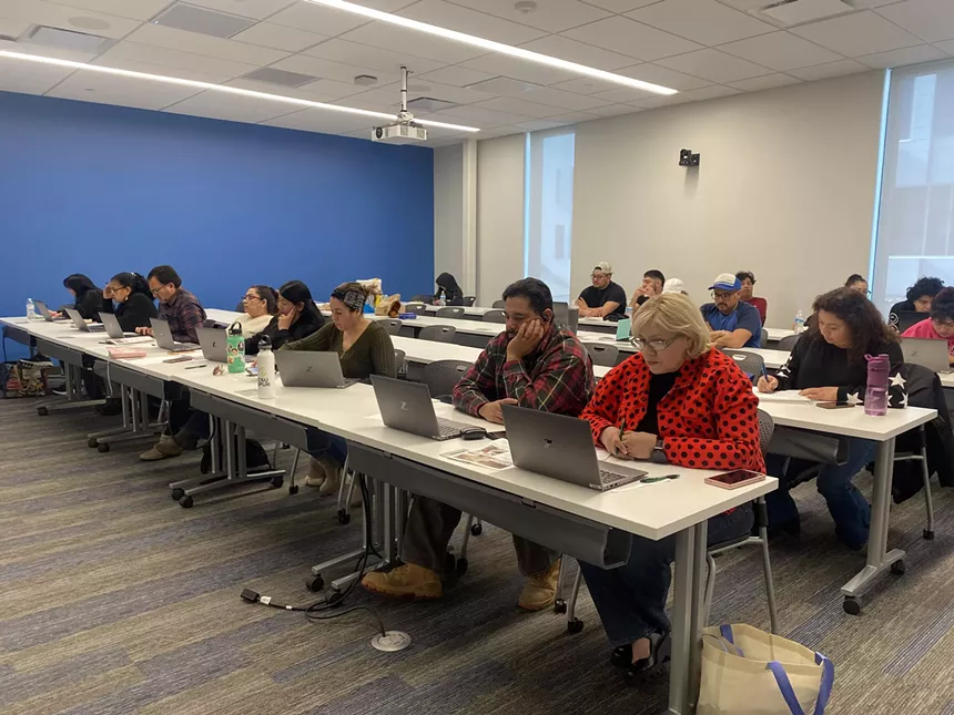 People seated at long white tables, each with a laptop
