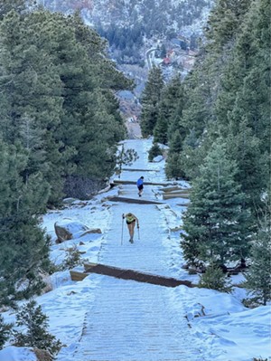 Erin Ton climbing up the snow-covered stairs of the Manitou Incline, wearing yellow and holding trekking poles.