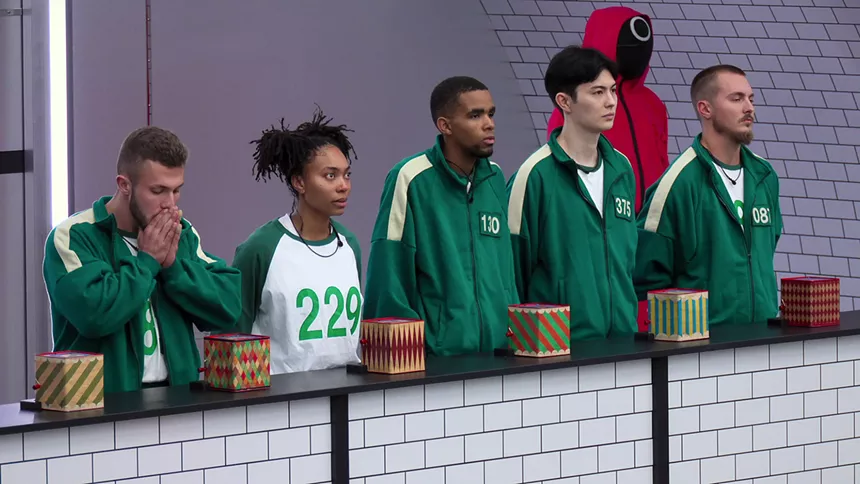 Five contestants lined up in front of a table with several jack-in-the-box games during Squid Game: The Challenge.