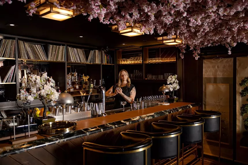 A woman making a cocktail behind the bar; its shelves are stocked with records