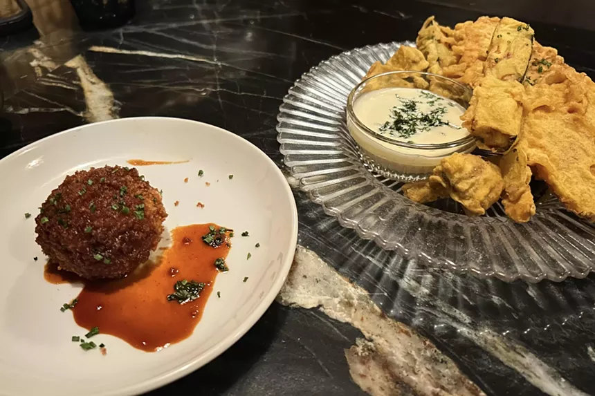 A potato croquette on a white plate and a dish of vegetable tempura