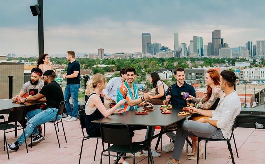 Groups of people dining on The Red Barber's rooftop, backdropped by the Denver skyline
