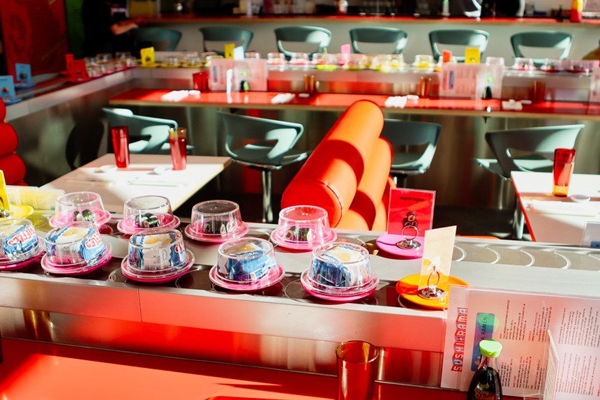 a conveyor belt with small dishes on it surrounding counter seating
