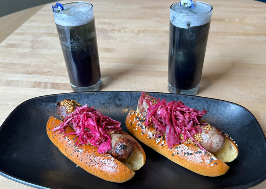 two brats topped with purple slaw in front of two purple cocktails