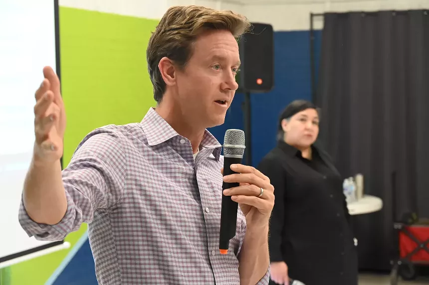 A man speaking with a woman listening the background.