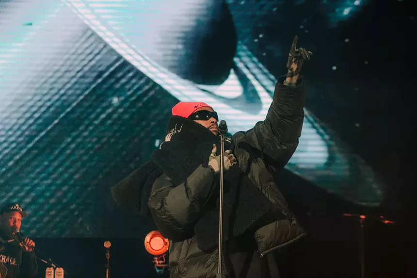 man in pink hat at a microphone with his hand in the air