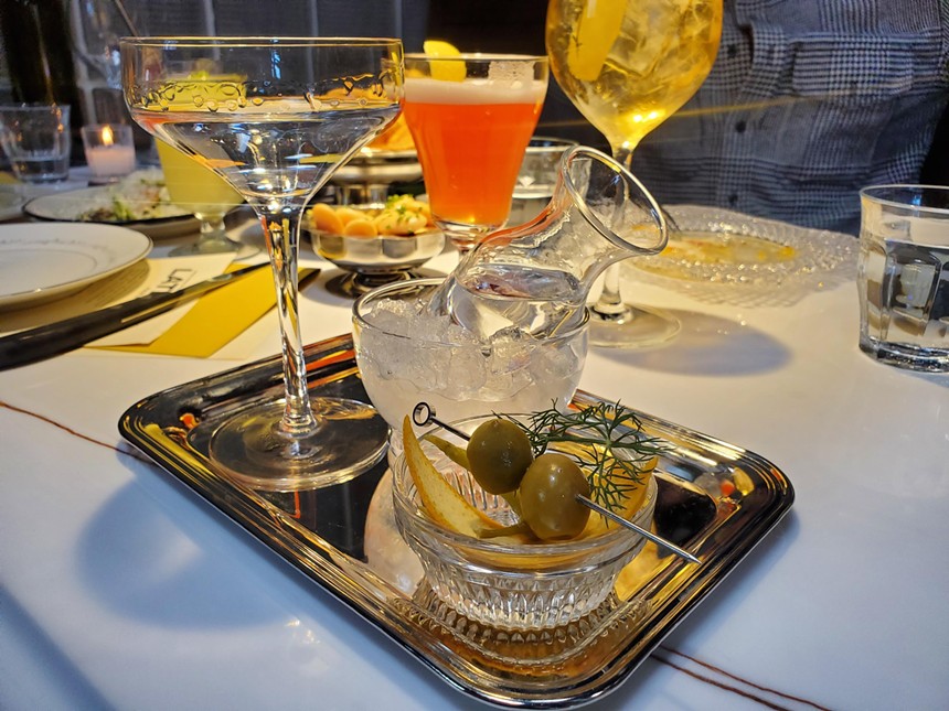 a martini on a silver tray with olives and lemon zest in a bowl