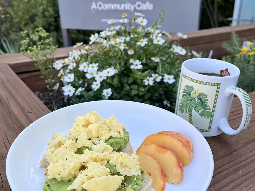 Avocado toast topped with scrambled eggs and a mug of coffee on a bench outside GraceFull Cafe