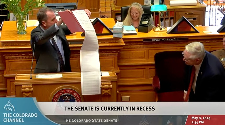 Senate Minority Leader Paul Lundeen holds a long paper in front of Senator Bob Gardner on the Senate floor.