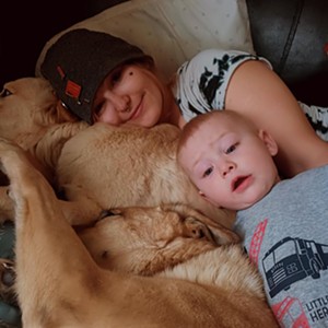 A woman laying down with her baby and dog.