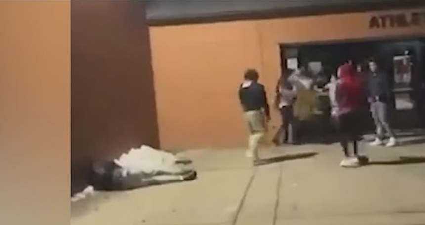 A young person lying on the ground during a fight outside a school.