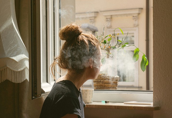 Woman blows smoke out open window