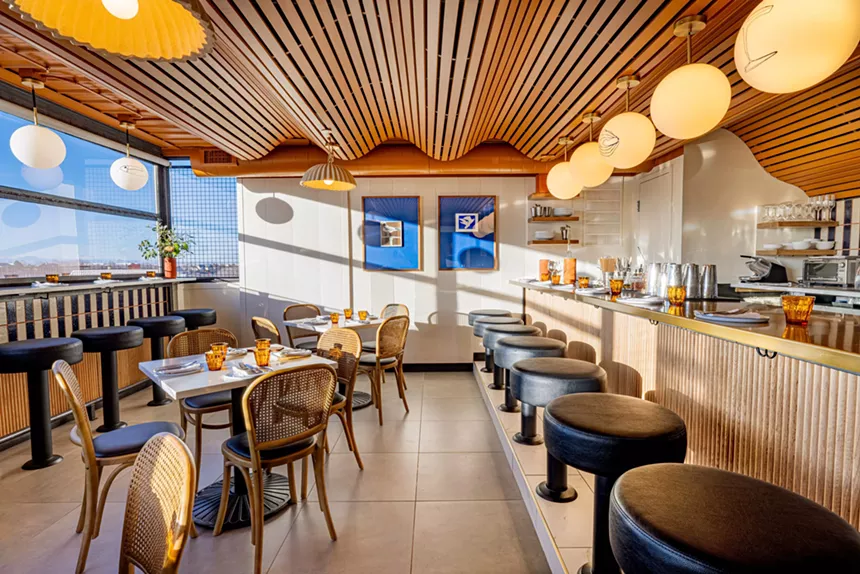 The interior of a bar with a wavy wood slat ceiling, globe pendant lights and a mid-century aesthetic