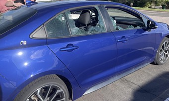 A blue car with two passenger-side windows shot out and a bullethole near the trunk.