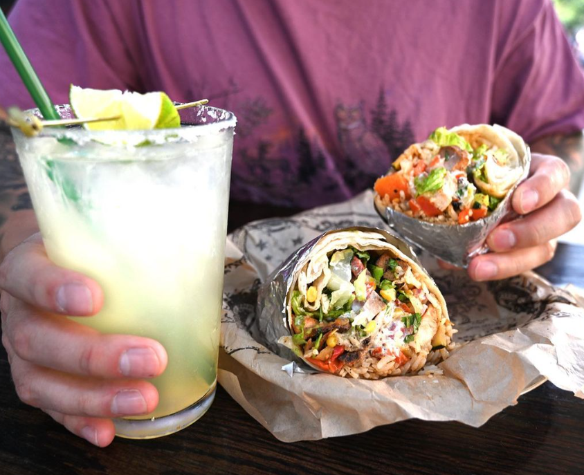 hands holding a margarita and a burrito