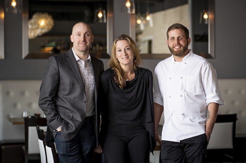man in a suit, woman in black shirt and man in white chef's coat posing