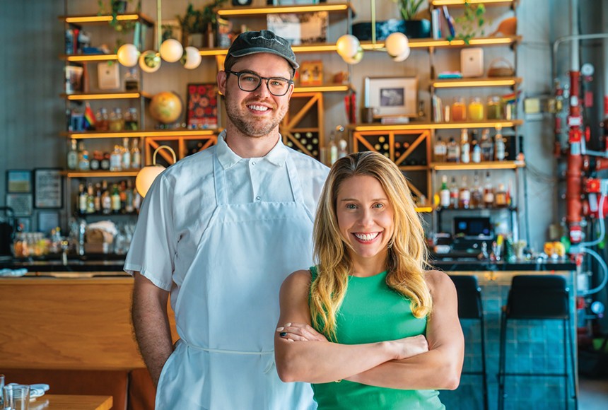 man in a chef's coat and apron posing next to a woman in a green shirt
