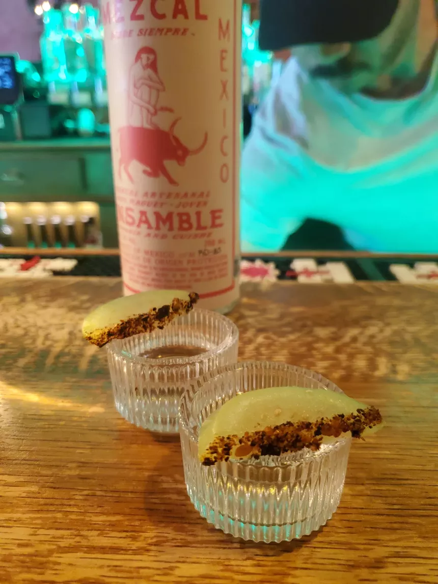 two shots of mezcal in glasses on a bar
