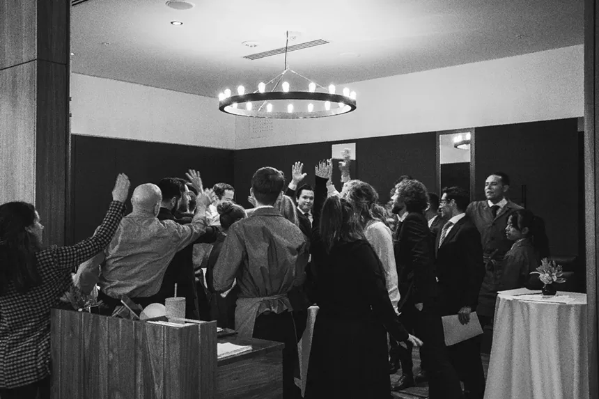 black and white photo of a group of people gathered in a circle in a dining room