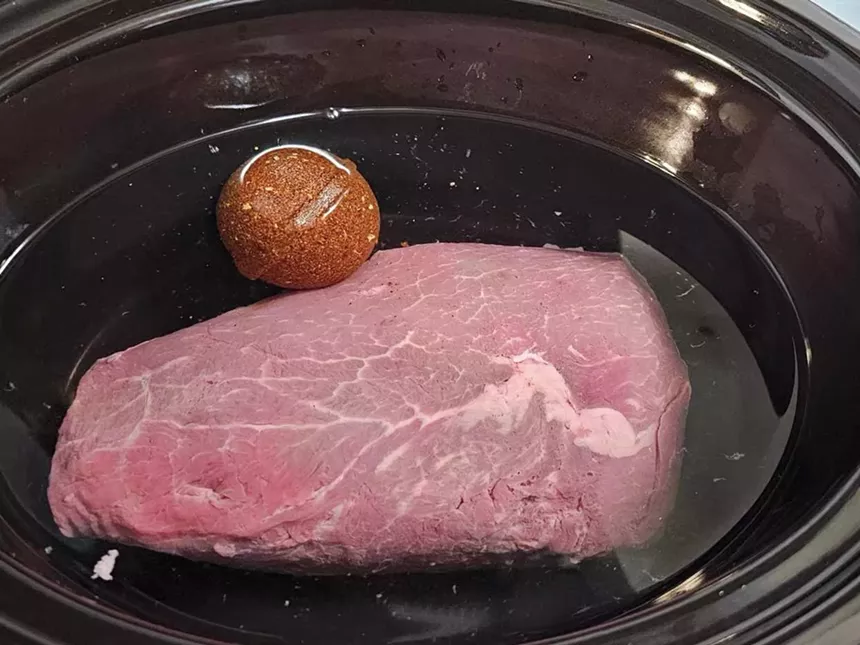 A large piece of meat, water and a Bombitas birria bomb inside a slow cooker