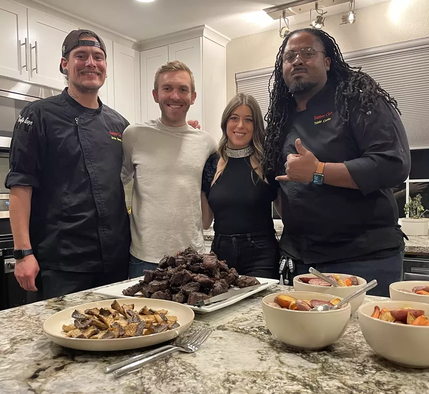 four people posing for a photo in front of plates of food