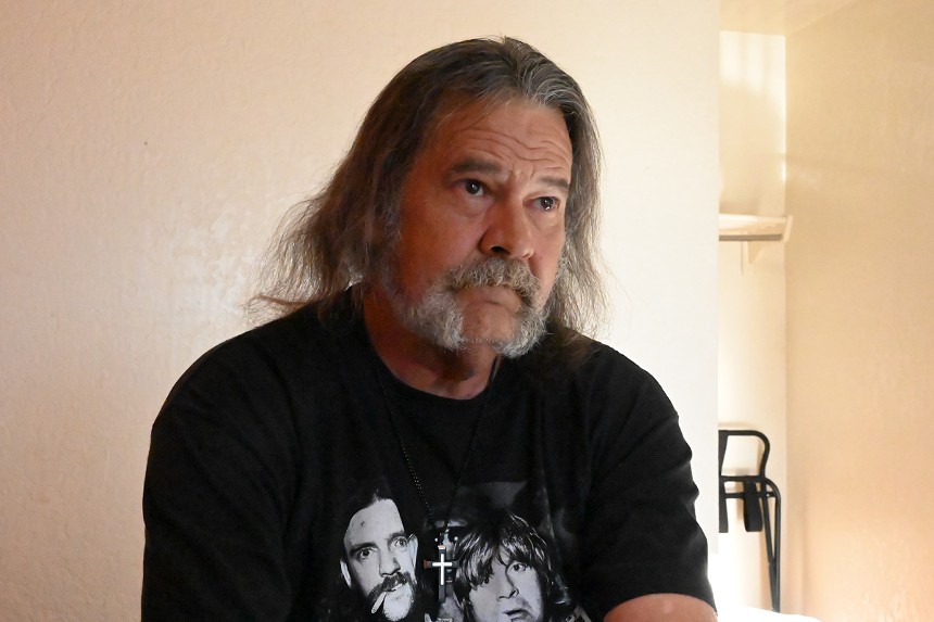 A man with long grey hair and a mustache stares.