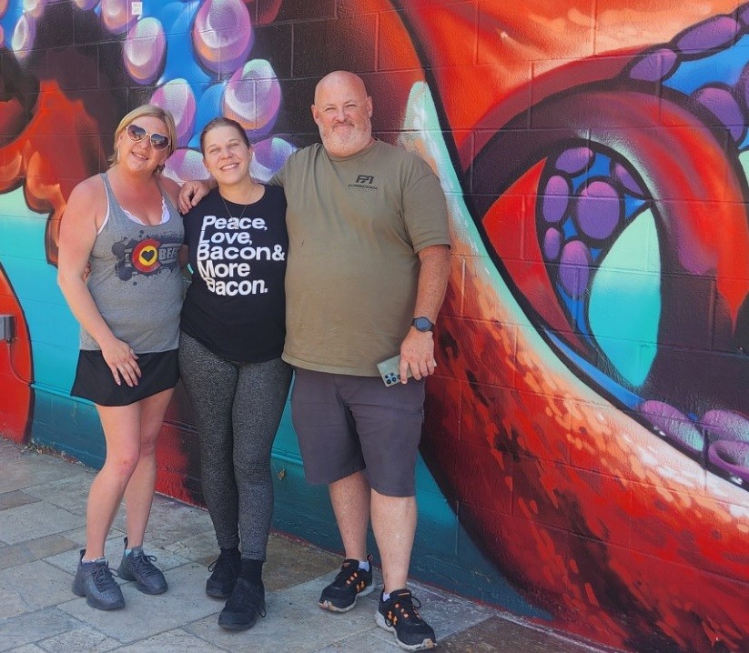 three people posing in front of a mural