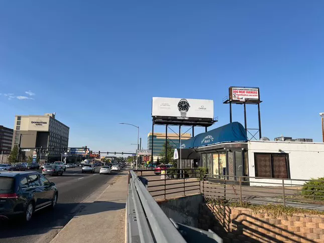 A billboard reads, "Denver slaughterhouse ban hurts dog meat farmers, ElwoodDogMeat.com/no309" with illustrations of a wiener dog running from a piece of steak. At the bottom, it says, "If this fake ad bothers you, ask yourself why."