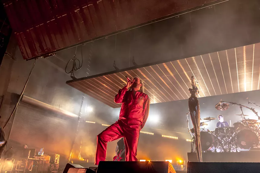 a man in a red jumpsuit standing in front of a stage holding a microphone.