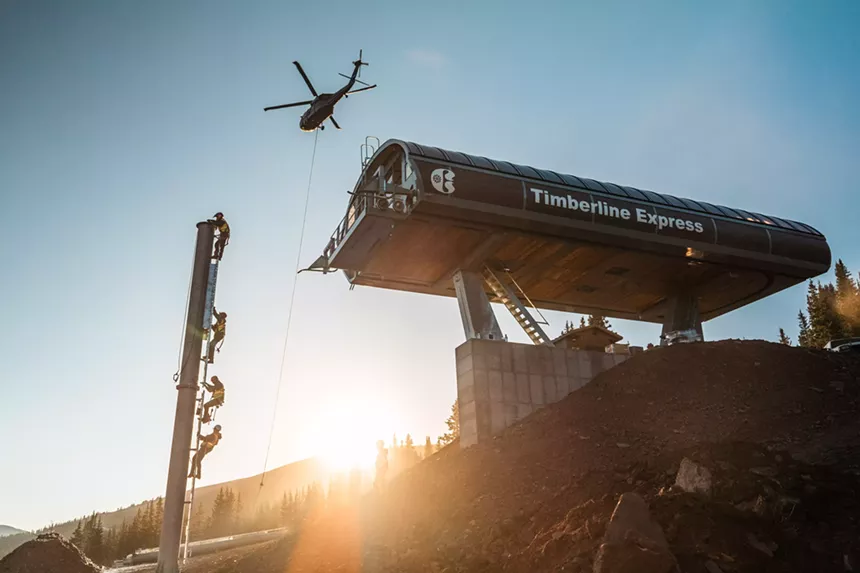 Workers on a ski lift tower and a helicopter flying above during the Timberline Express installation