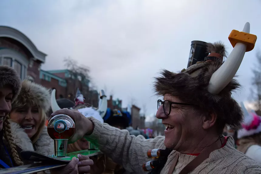 Litch Polich in a Viking helmet pouring bourbon into a shotski cup