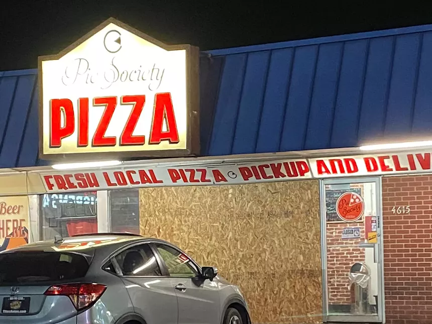 front of pizzeria with a window boarded up