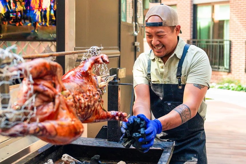 man in an apron cooking a whole pig on a spit