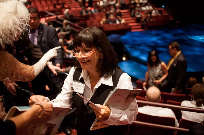 An usher looks at a paper ticket to help a patron find their seat.
