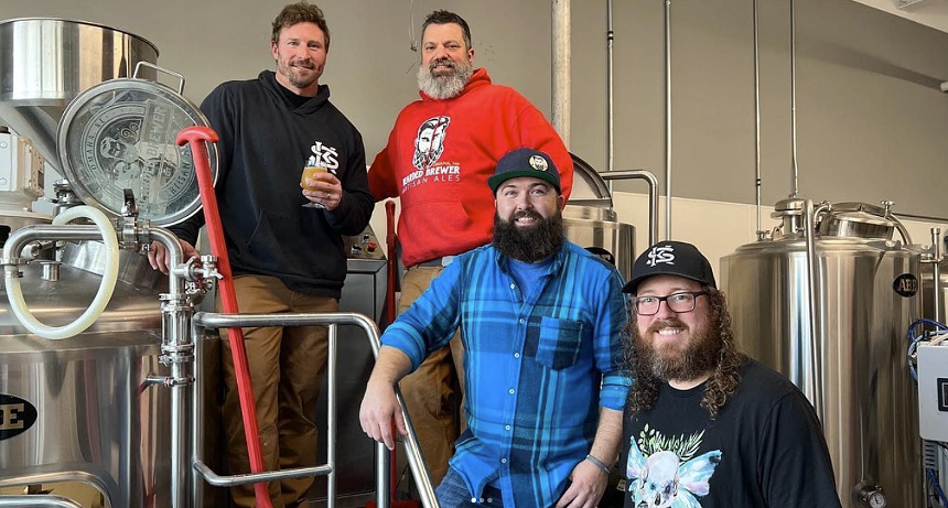 Group of men posing on brewery equipment.