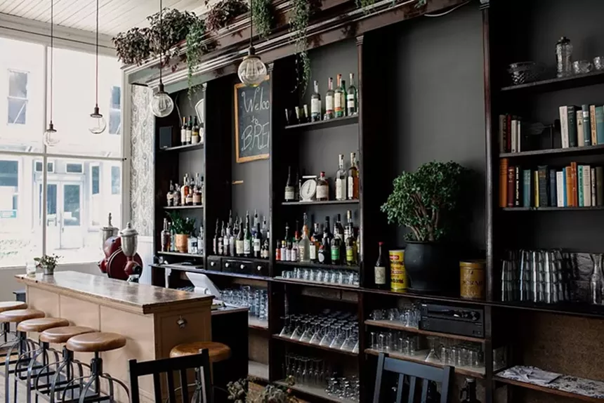 The interior of Bread Bar, featuring wood stools and liquor bottles on black shelving