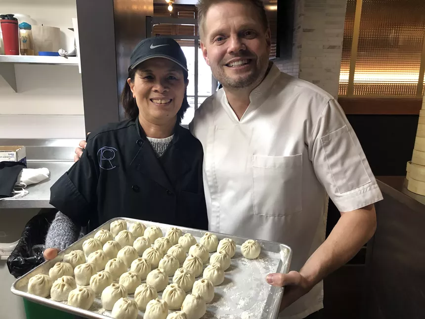 two chefs holding a tray of dumplings