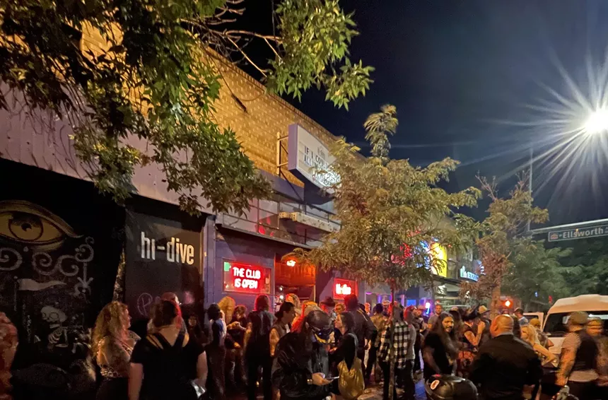 Patrons standing outside of hi-dive's iconic neon sign that reads "The Club is Open."