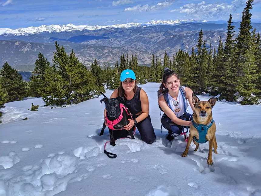 Hyak, Nichols and two dogs posed in the snow and backdropped by mountains